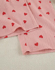 Cotton pajama fabric in soft pink with red heart patterns for a cozy nightwear look.