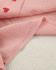 Close-up of soft pink cotton fabric with red heart prints, showcasing delicate craftsmanship and texture.